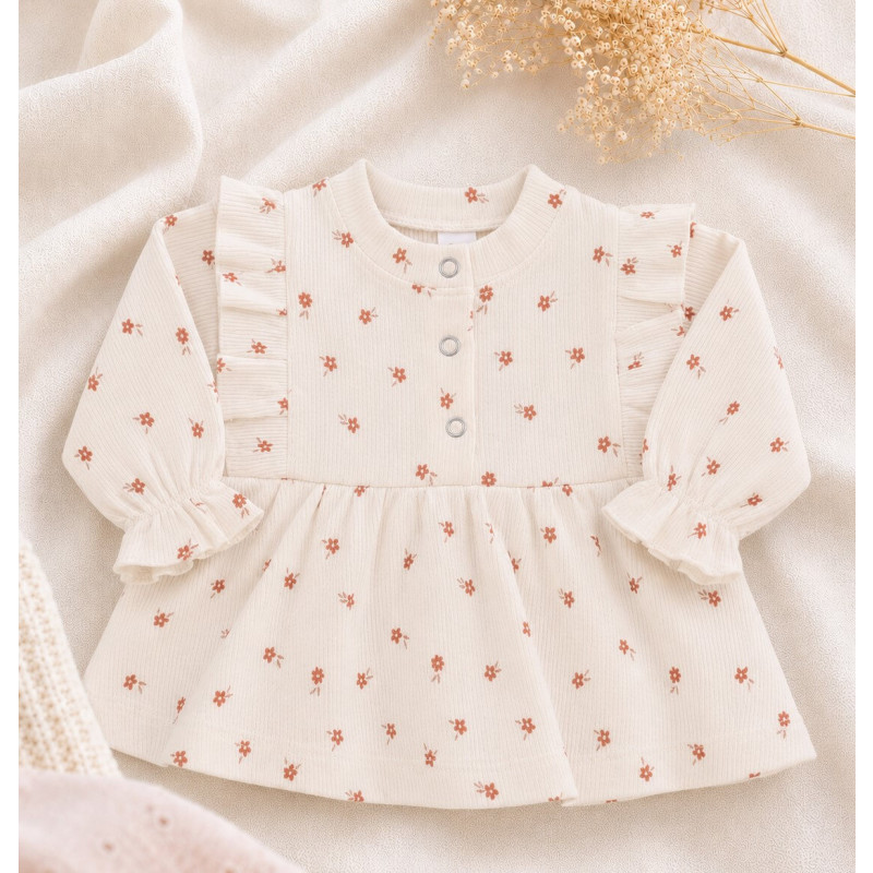 Een newborn blousje met ruffles langs de schouders en een printje van roze bloemetjes.