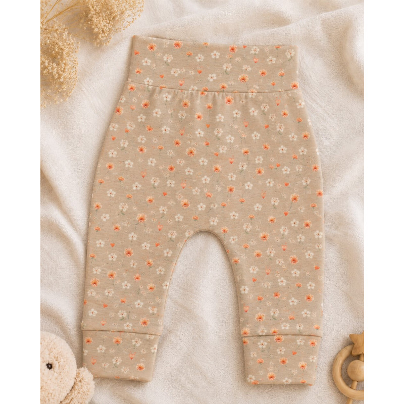 Een zandkleurig newborn broekje met kleine oranje bloemetjes en hartjes.