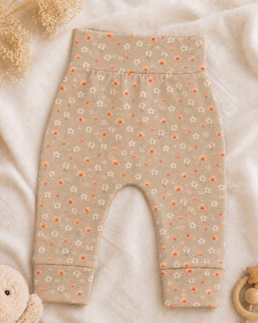 Een zandkleurig newborn broekje met kleine oranje bloemetjes en hartjes.